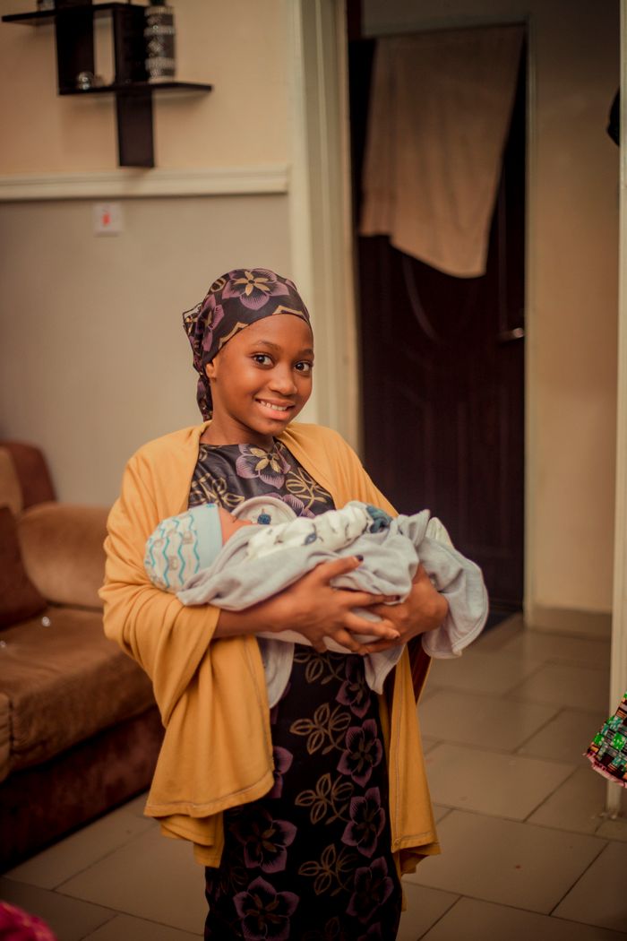 A happy mother holding her newborn baby, captured in a warm indoor setting.